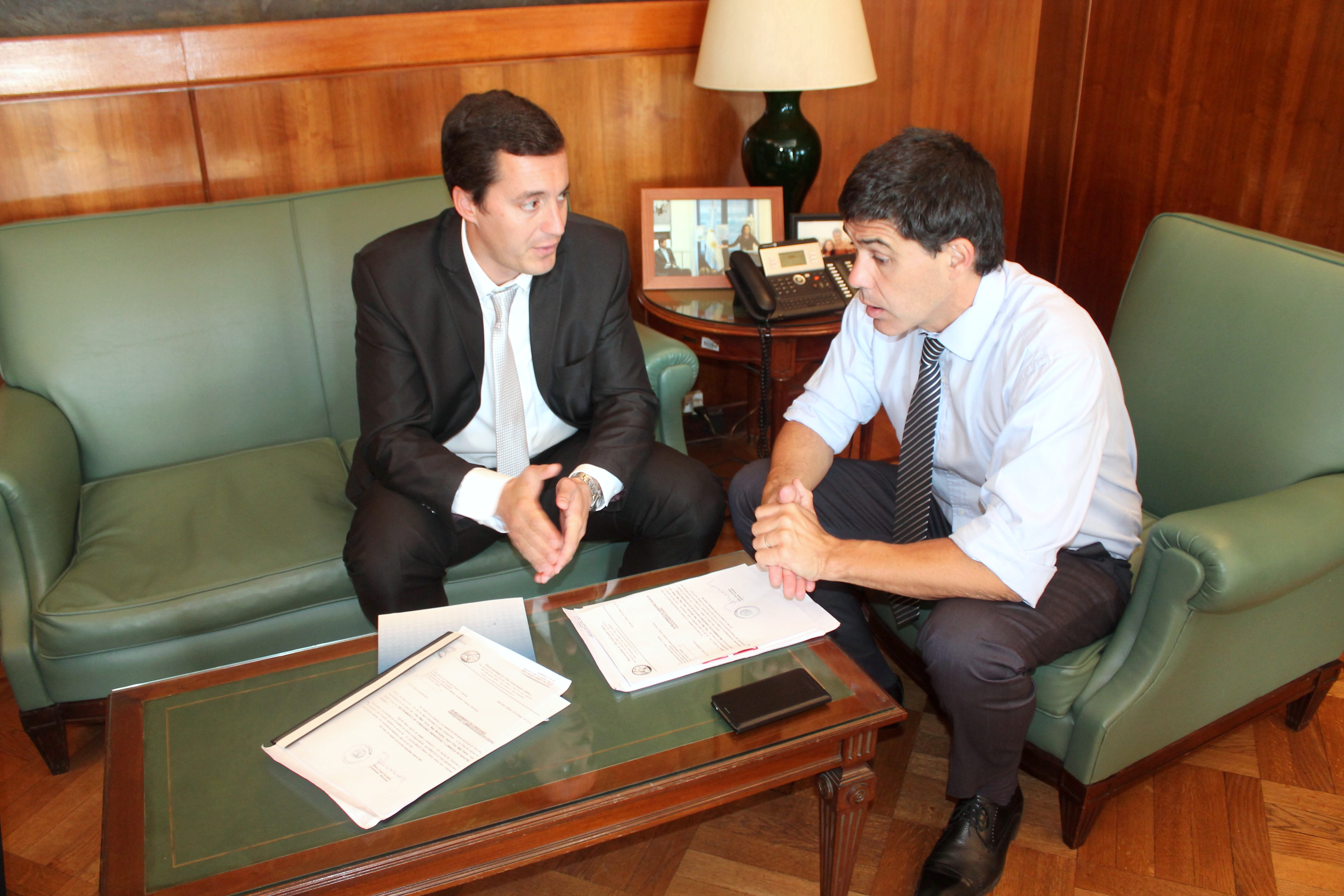 Dos personas conversan sentadas junto a una mesa con documentación.