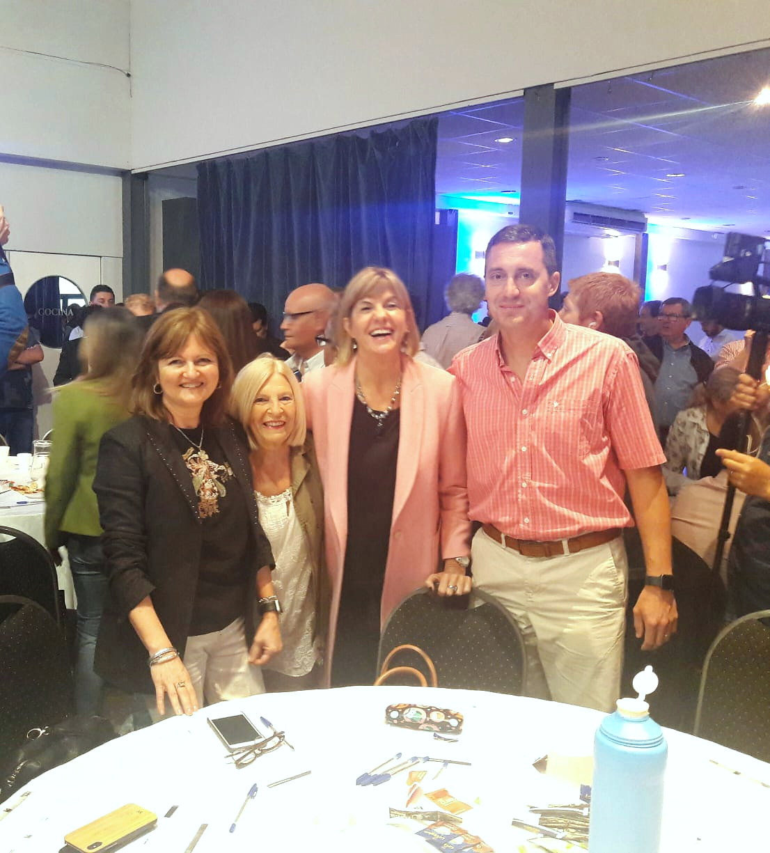 Cuatro personas posan juntas en un salón con público.