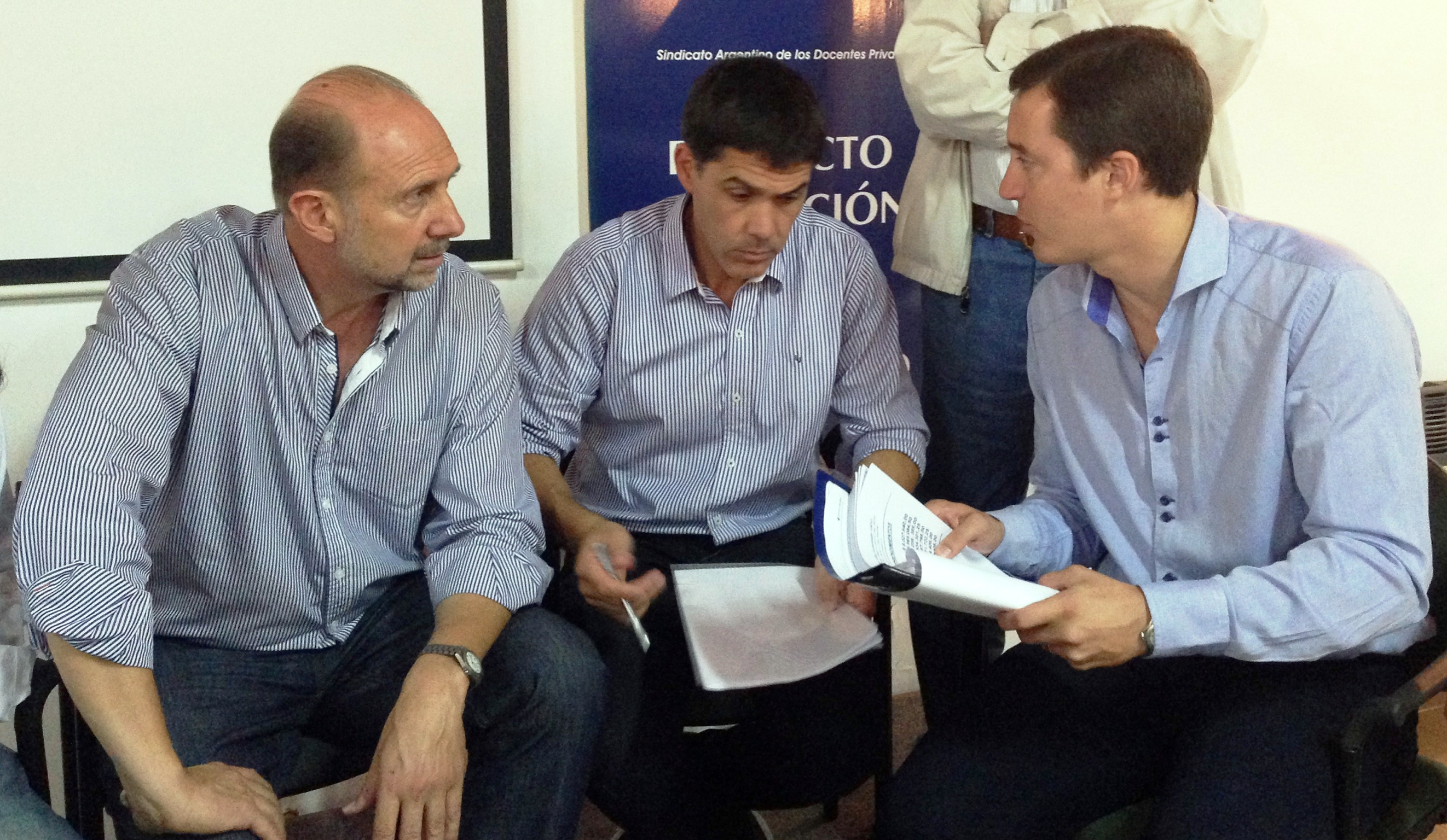Tres personas conversan con documentación en las manos.