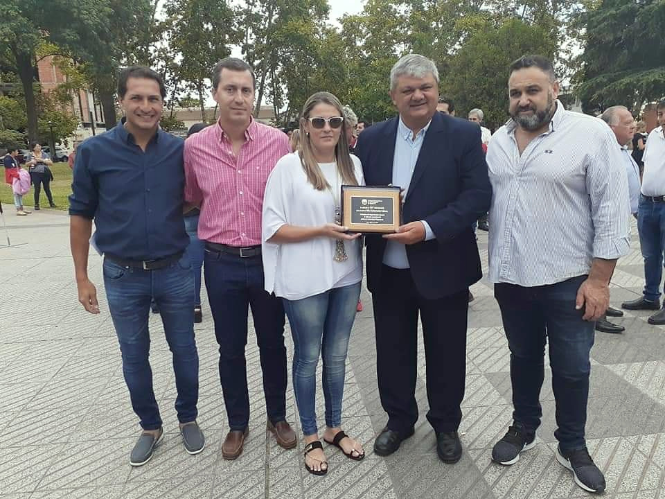Cinco personas posan en un espacio público; dos sostienen una placa.