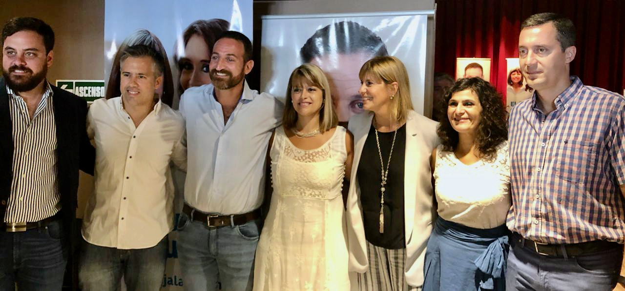Siete personas posan juntas frente a carteles en un salón.