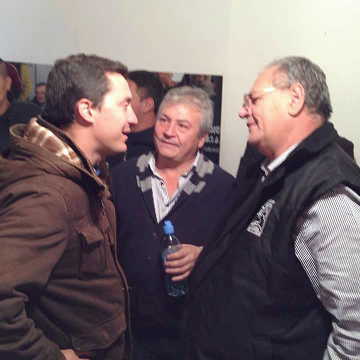 Tres personas conversan de pie en un encuentro en un ambiente interior.